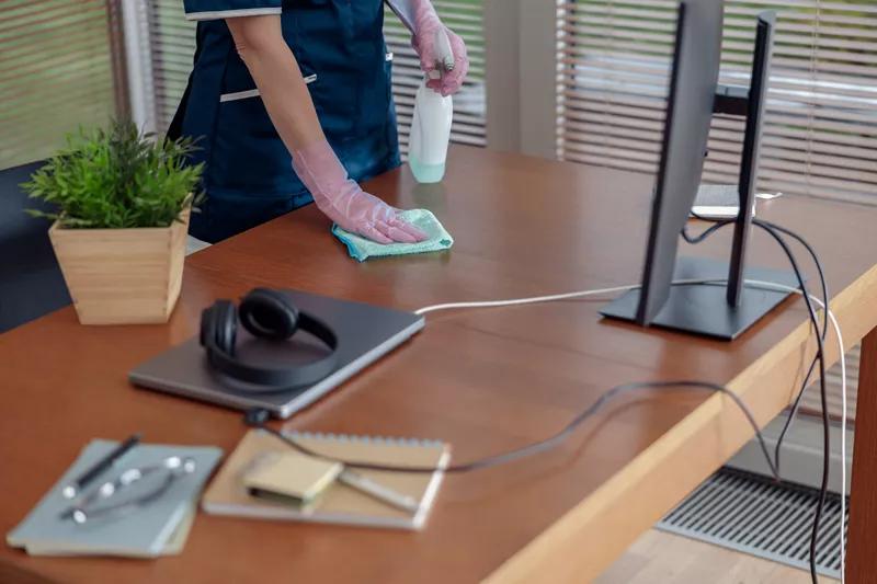 Bild zeigt Reinigungskraft von Clean Management Bernd Bürkle beim Wischen eines Schreibtisches im Büro